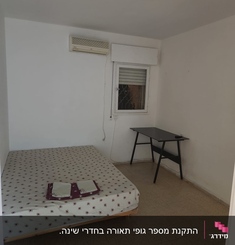 מזגן תלוי על הקיר בחדר ריק עם מיטה ושולחן